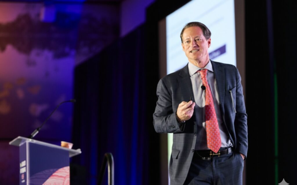 man in suit speaking to an audience on stage
