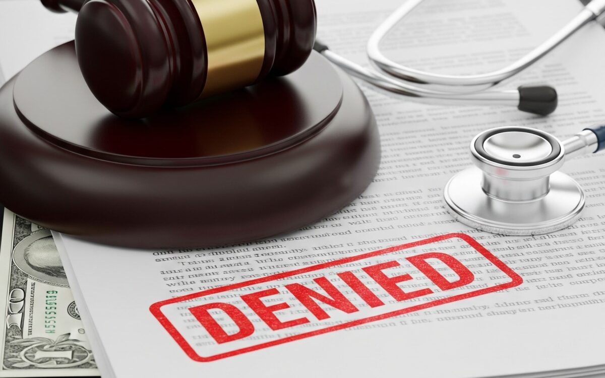 Conceptual image of a medical stethoscope, a legal gavel, and health insurance paperwork stamped with a red 'DENIED' mark, representing hospital revenue cycle strain.