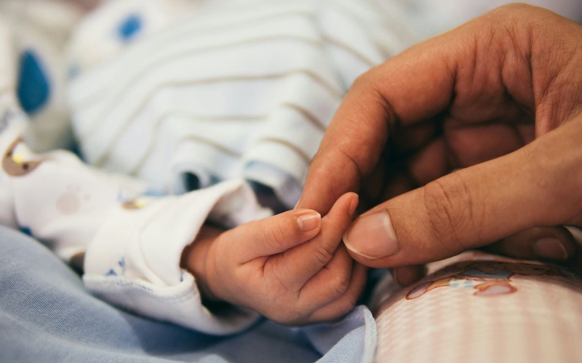 Paediatric clinical trials: newborn baby gripping adult finger in hospital