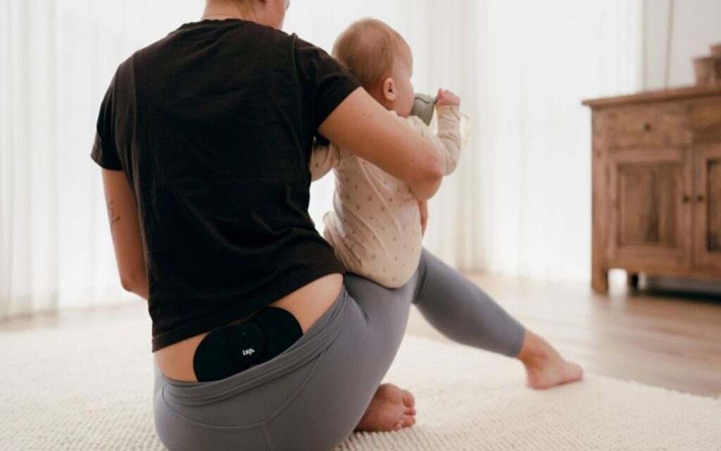 Person using a wearable TENS device for pelvic pain while caring for a baby at home