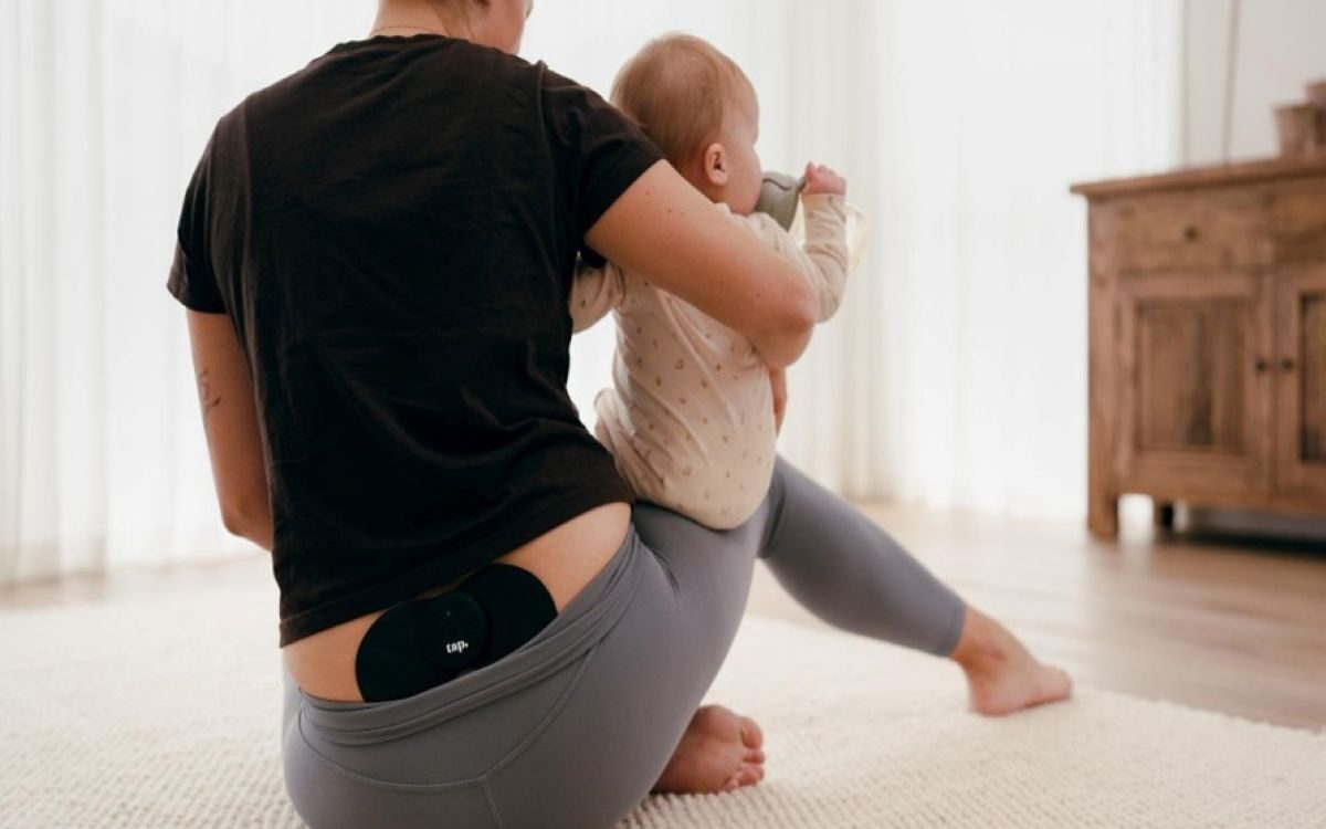 Person using a wearable TENS device for pelvic pain while caring for a baby at home