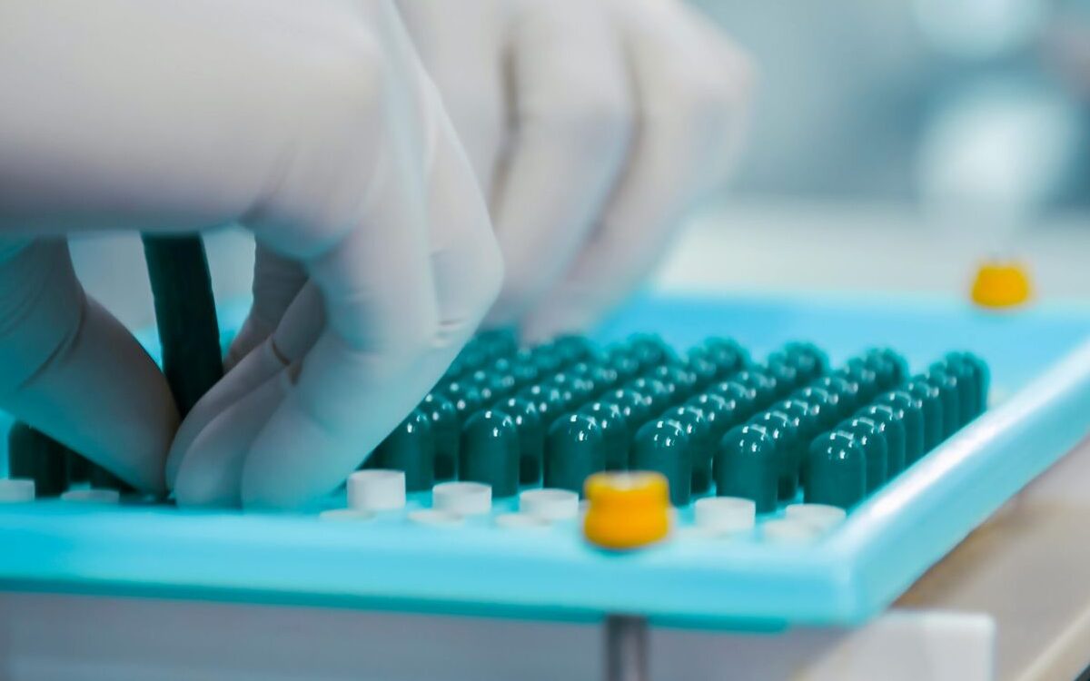 Biotech execution: gloved hands arranging pharmaceutical capsules in a drug manufacturing tray