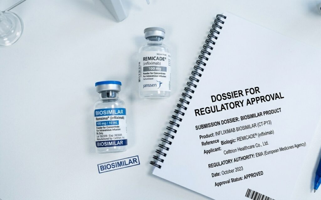 A biosimilar medication vial in focus in the foreground alongside an originator biologic vial and a regulatory approval document on a clinical white laboratory surface.
