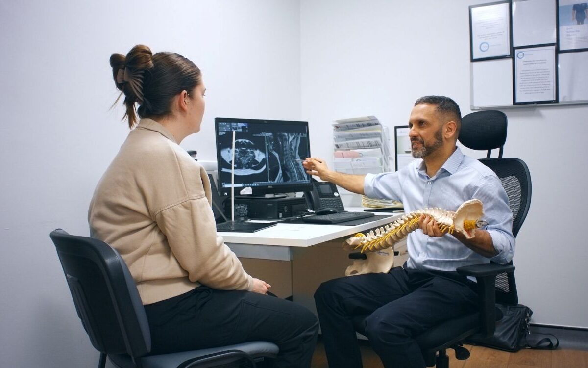 Spinal neurosurgeon explaining symptom-led spinal care to a patient using a spine model and MRI scans
