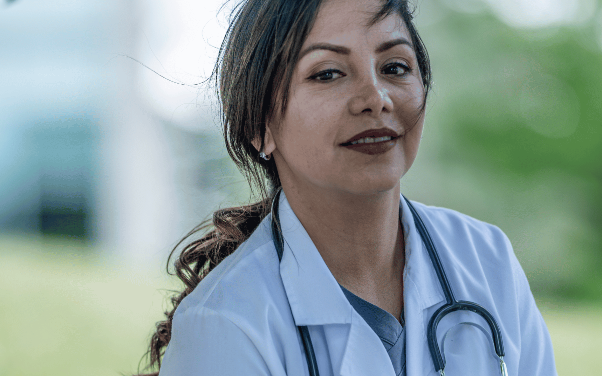 Female doctor in white coat and stethoscope pausing outdoors, reflecting on healthcare self-care