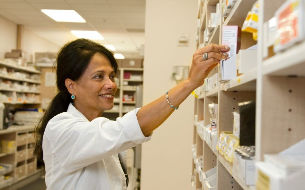 Pharmacist selecting medication from pharmacy shelves where manual PGD processes slow clinical workflows