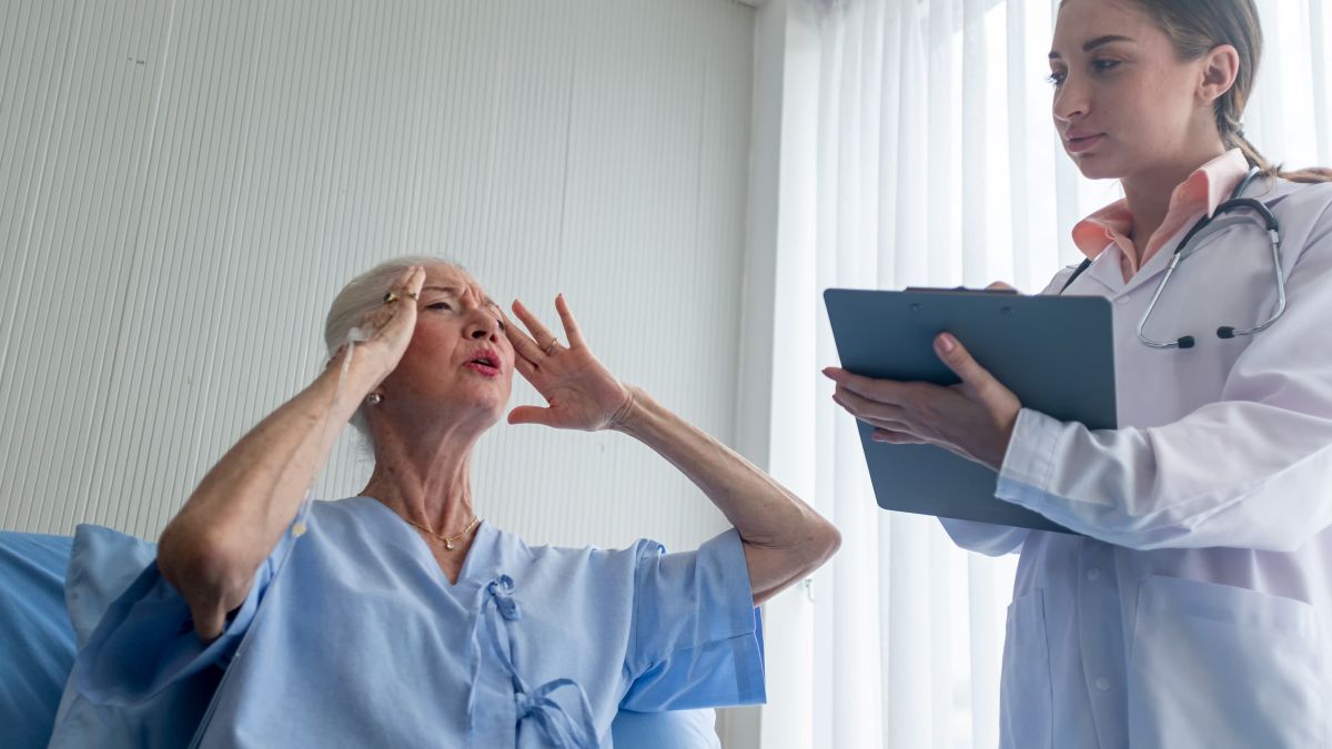 female-doctor-advising-patient-in-hospital-office-2026-03-18-07-09-44-utc-1 Older patient in a hospital bed gestures in distress as a clinician listens, a scenario calling for trauma-informed care.