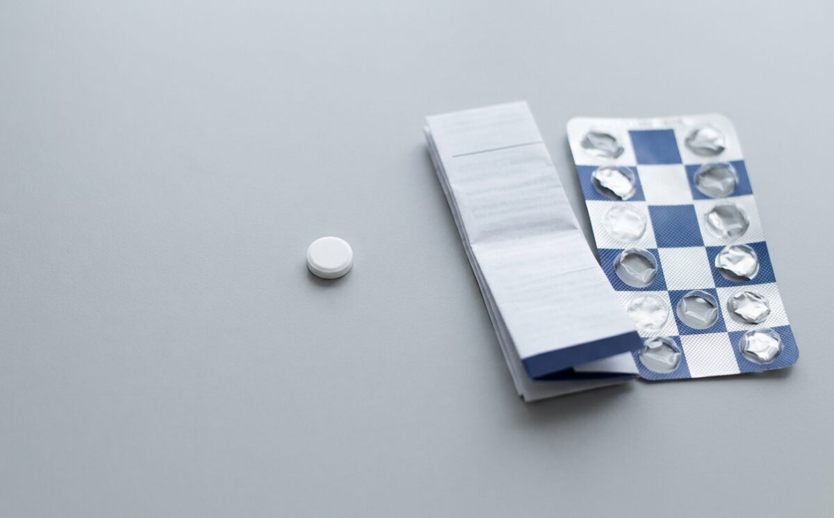 tablet-with-pack Single white tablet, blister pack and folded patient leaflet on grey, illustrating the brepocitinib dermatomyositis approval.